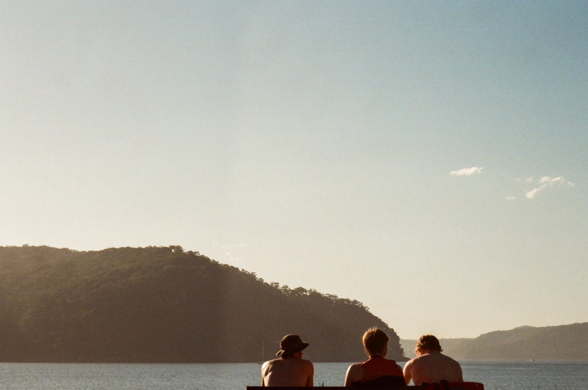 Three people on a bench, backs to the camera, headland and water