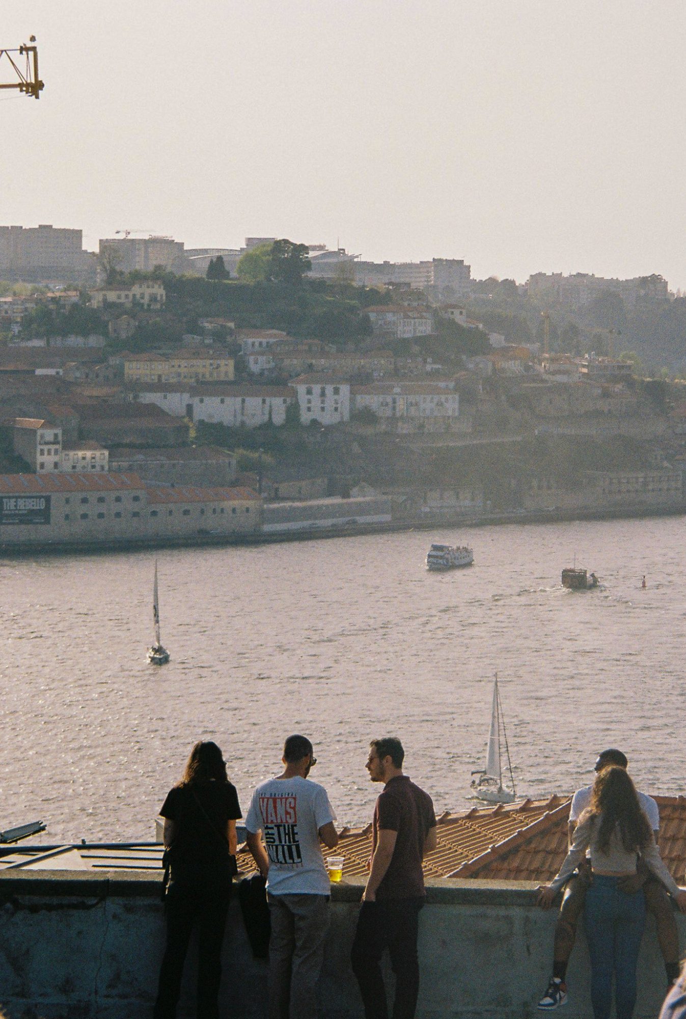 People leaning on a wall above the river, boats and the far bank