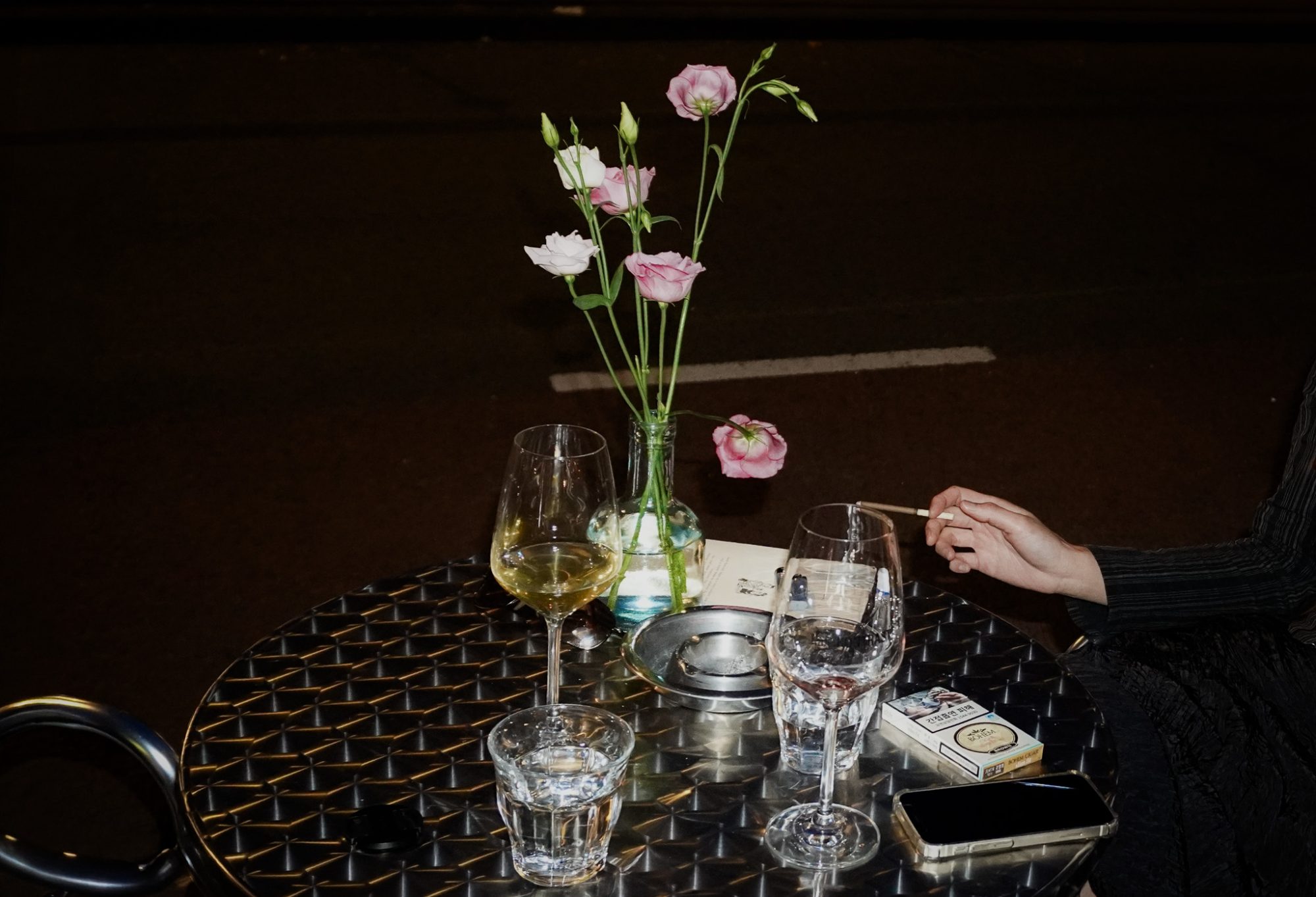 A hand with a cigarette at a night table, lisianthus in a bottle