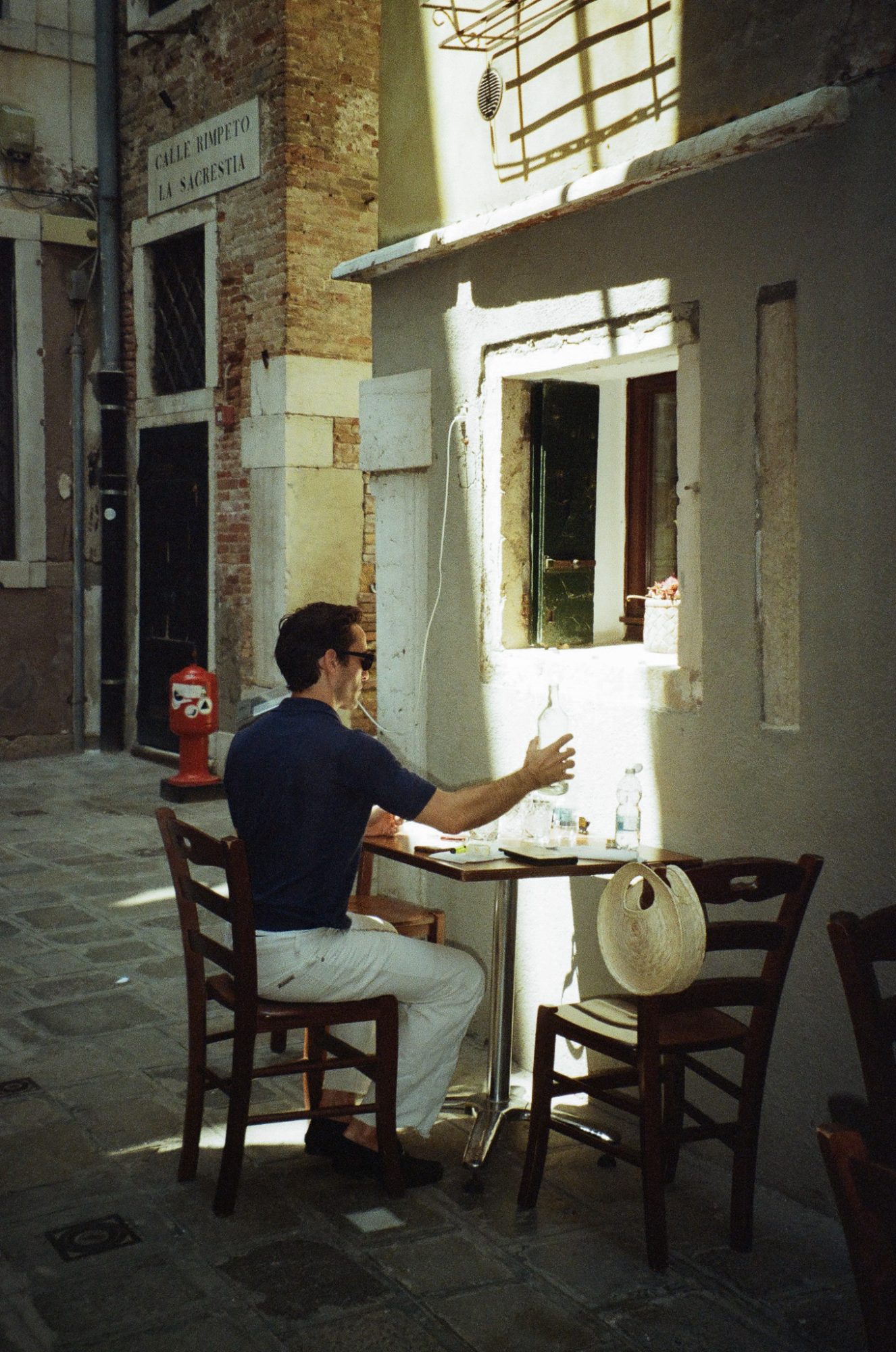A man at a café table reaching for a bottle, Calle Rimpeto la Sacrestia