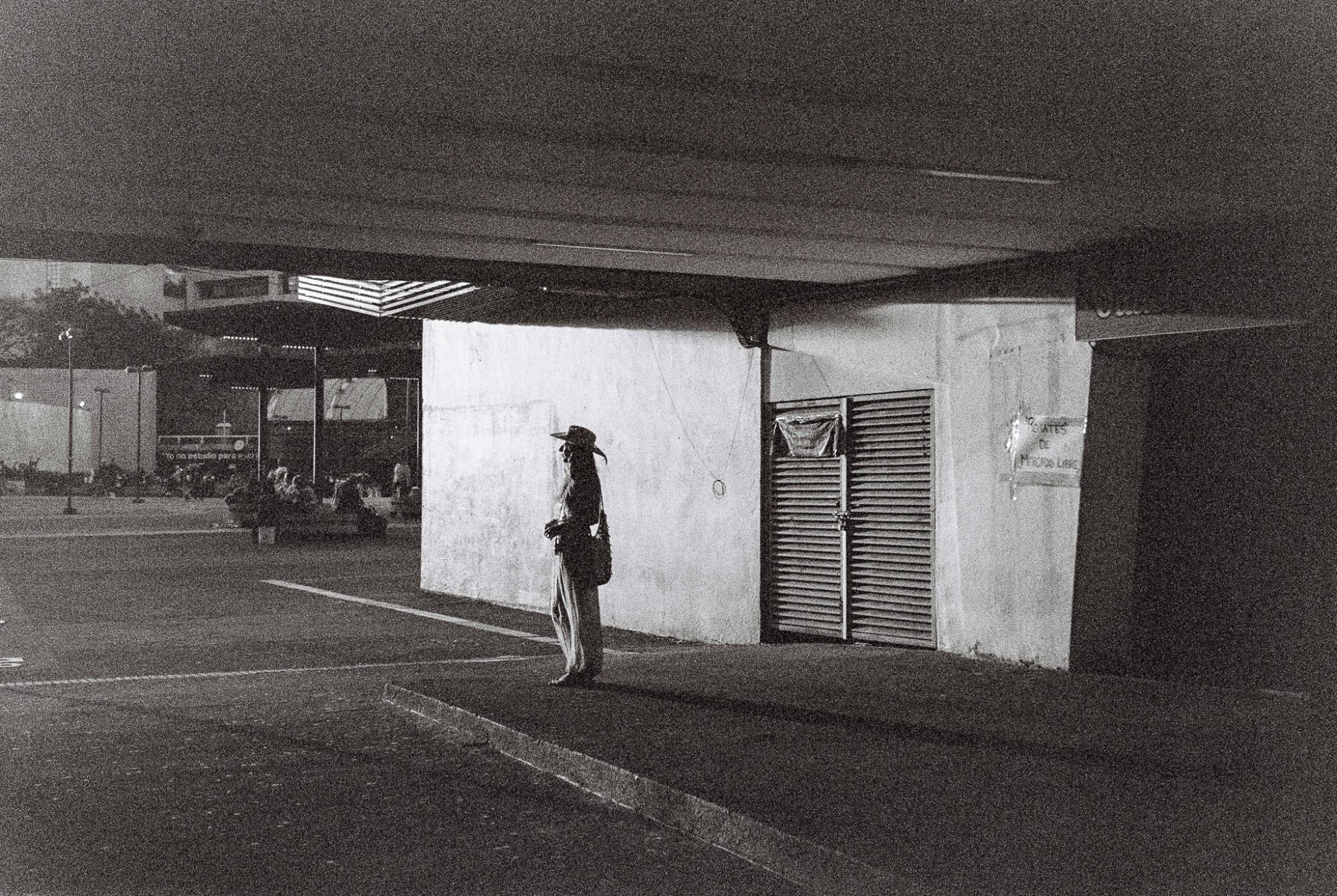 A woman waiting at a lit corner under a canopy, at night