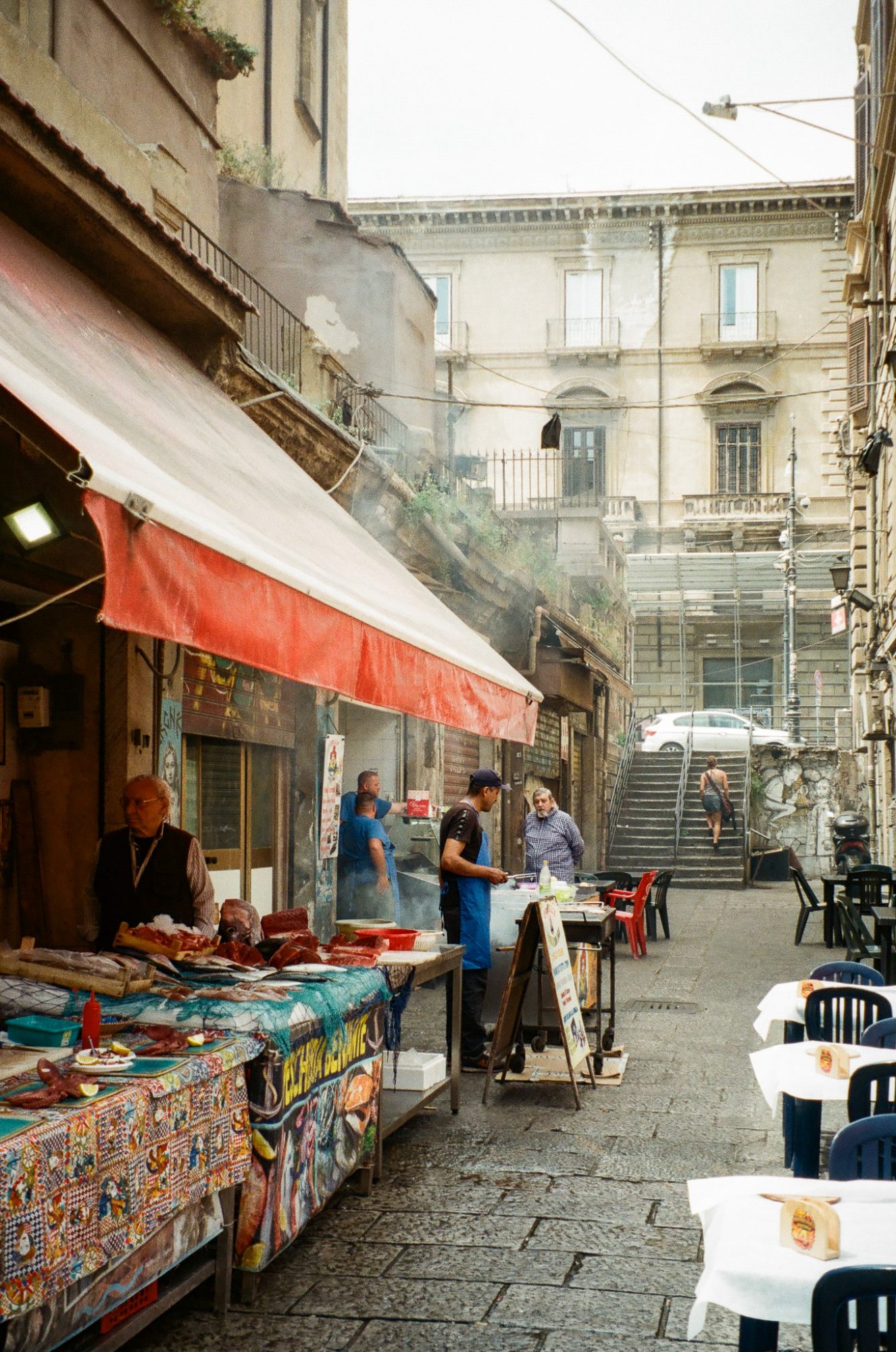 A fish stall under a red awning, smoke and stairs behind