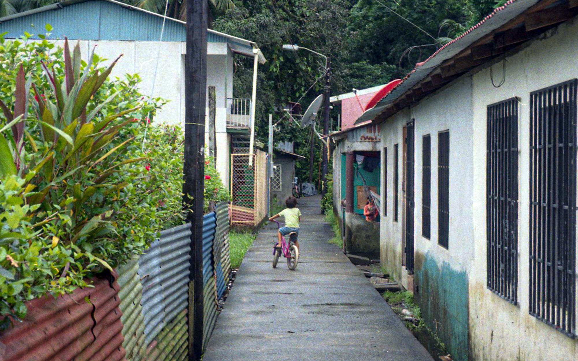 A boy cycling down a narrow alley between houses
